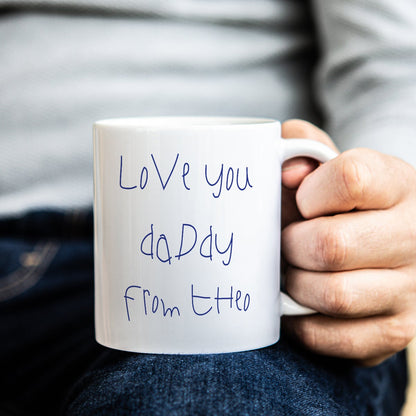 Person holding a white mug with 'Love you Daddy' in childs own handwriting
