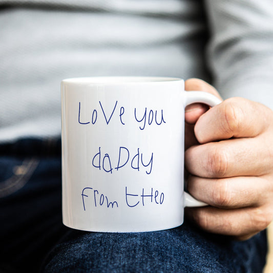 Person holding a white mug with 'Love you Daddy' in childs own handwriting