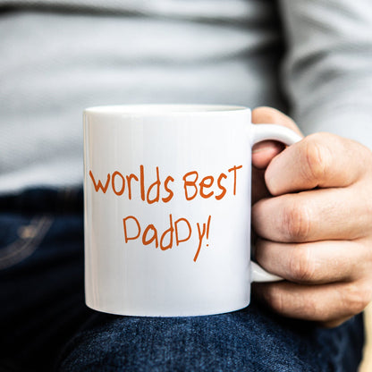 Person holding a white mug with 'Worlds Best Dad' text, in childs own handwriting