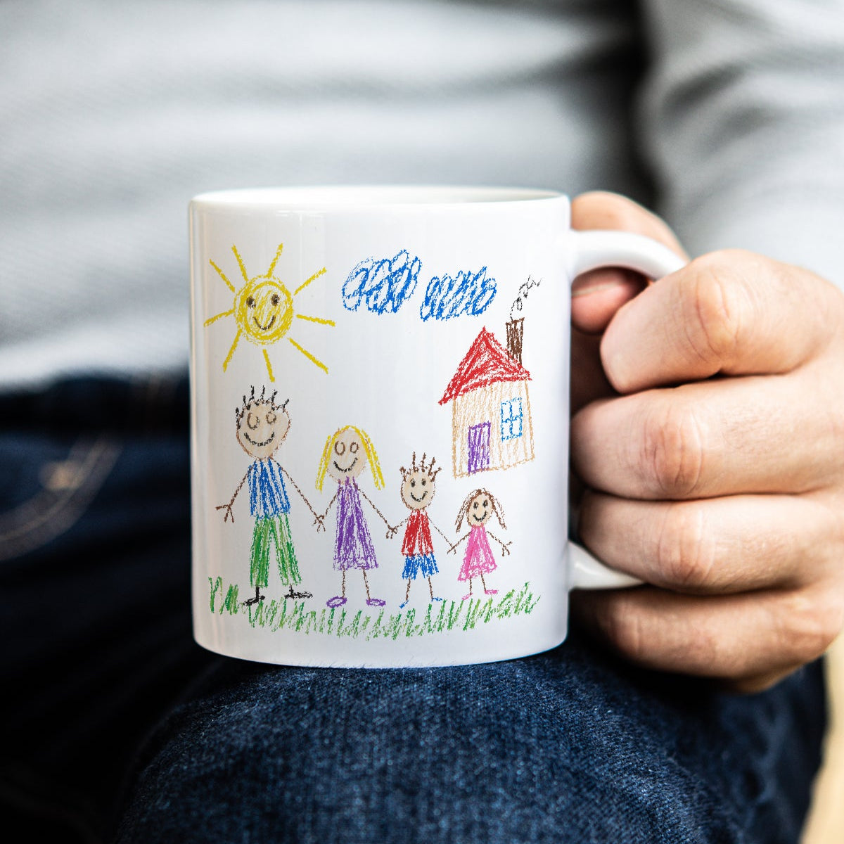 Person holding a mug with a child's drawing of a family and sun.
