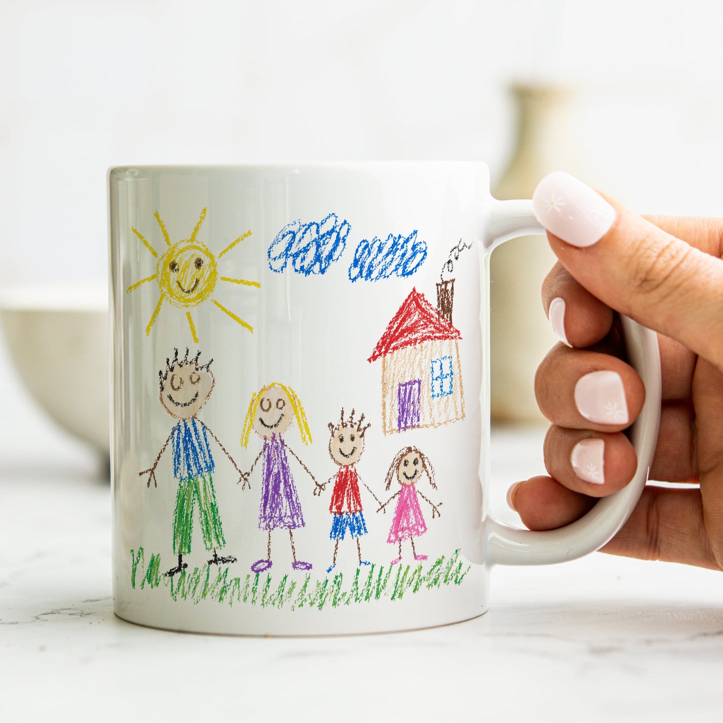 Hand holding a mug with a child's drawing of a family and sun.